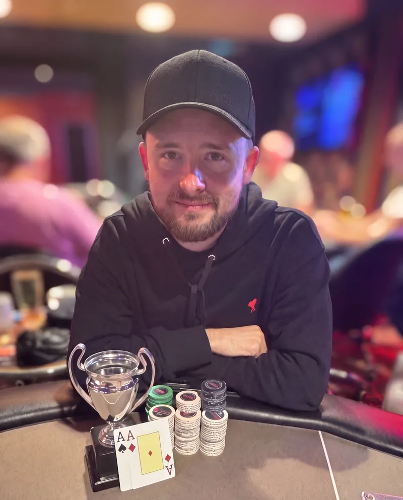 Tom Howcroft seated at a poker table with a small silver trophy and neat upright stacks of chips
