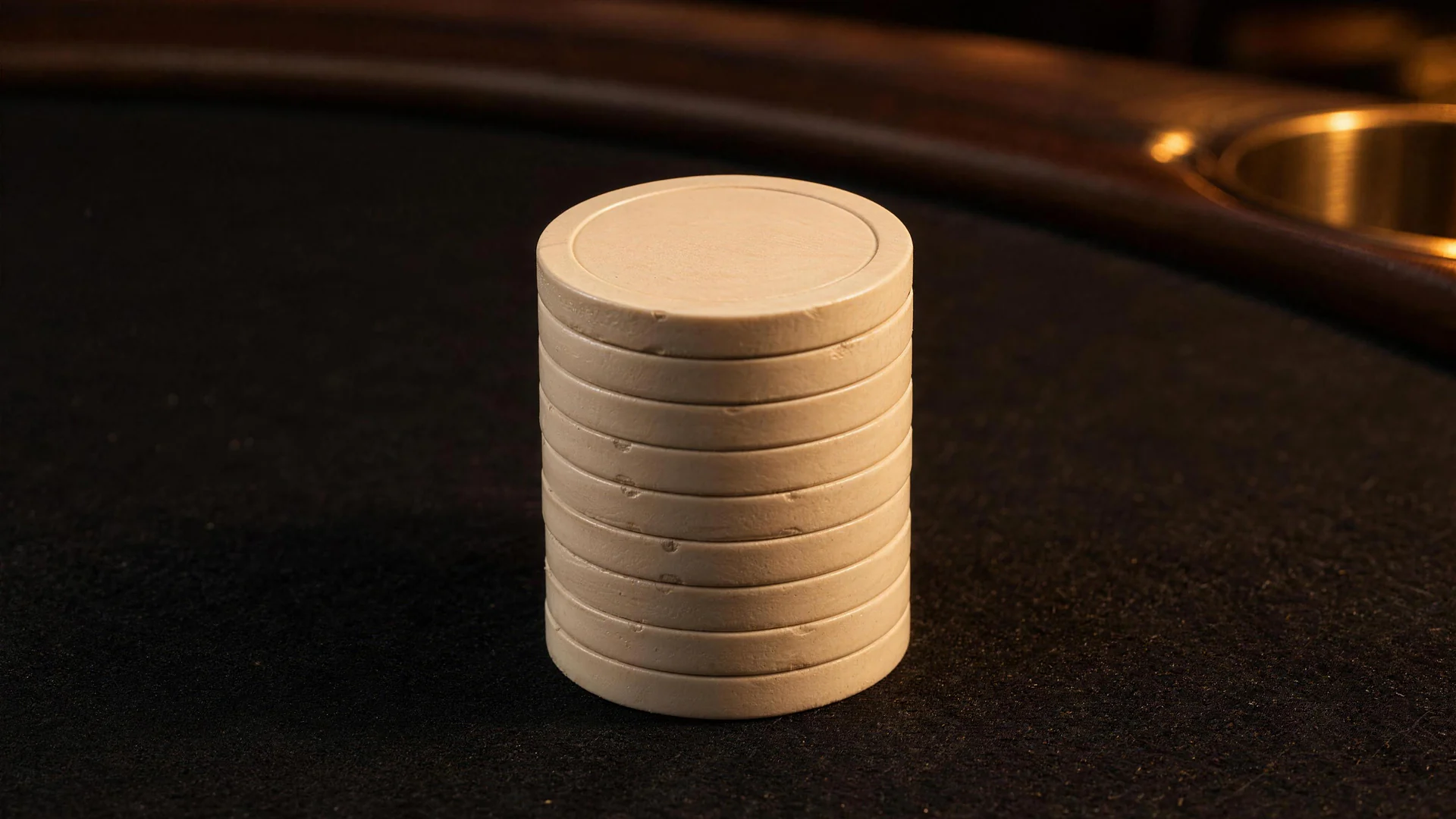 An ivory chip stack stands on dark poker felt, with a brass cup holder set into the rail behind