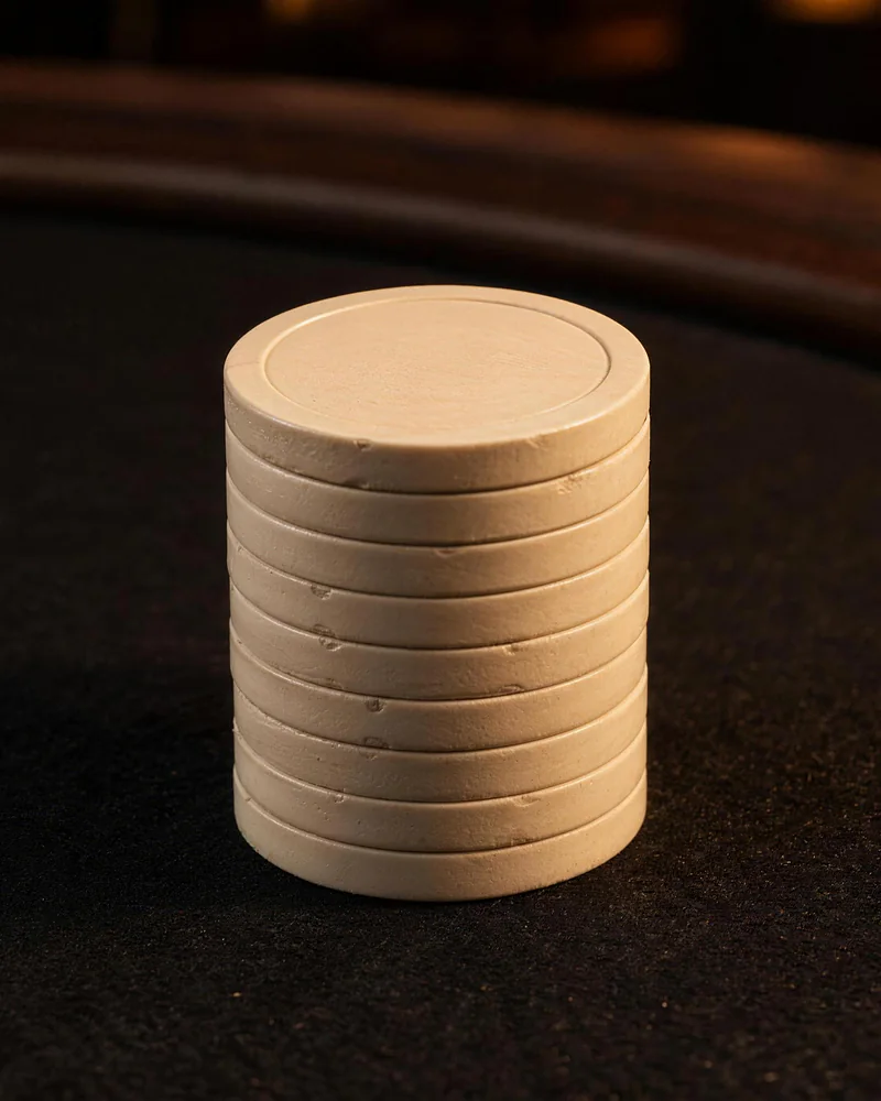 Small scuffs along pale chip edges Pale poker chips form an upright stack with small scuffs along their edges on dark felt